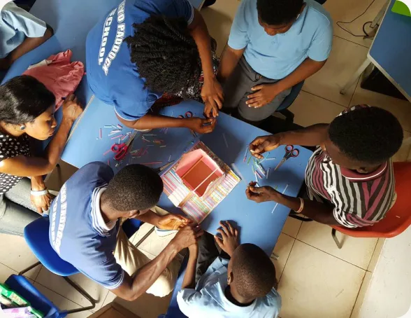 Children and a teacher working together on a hands-on craft activity around a blue table, seen from above